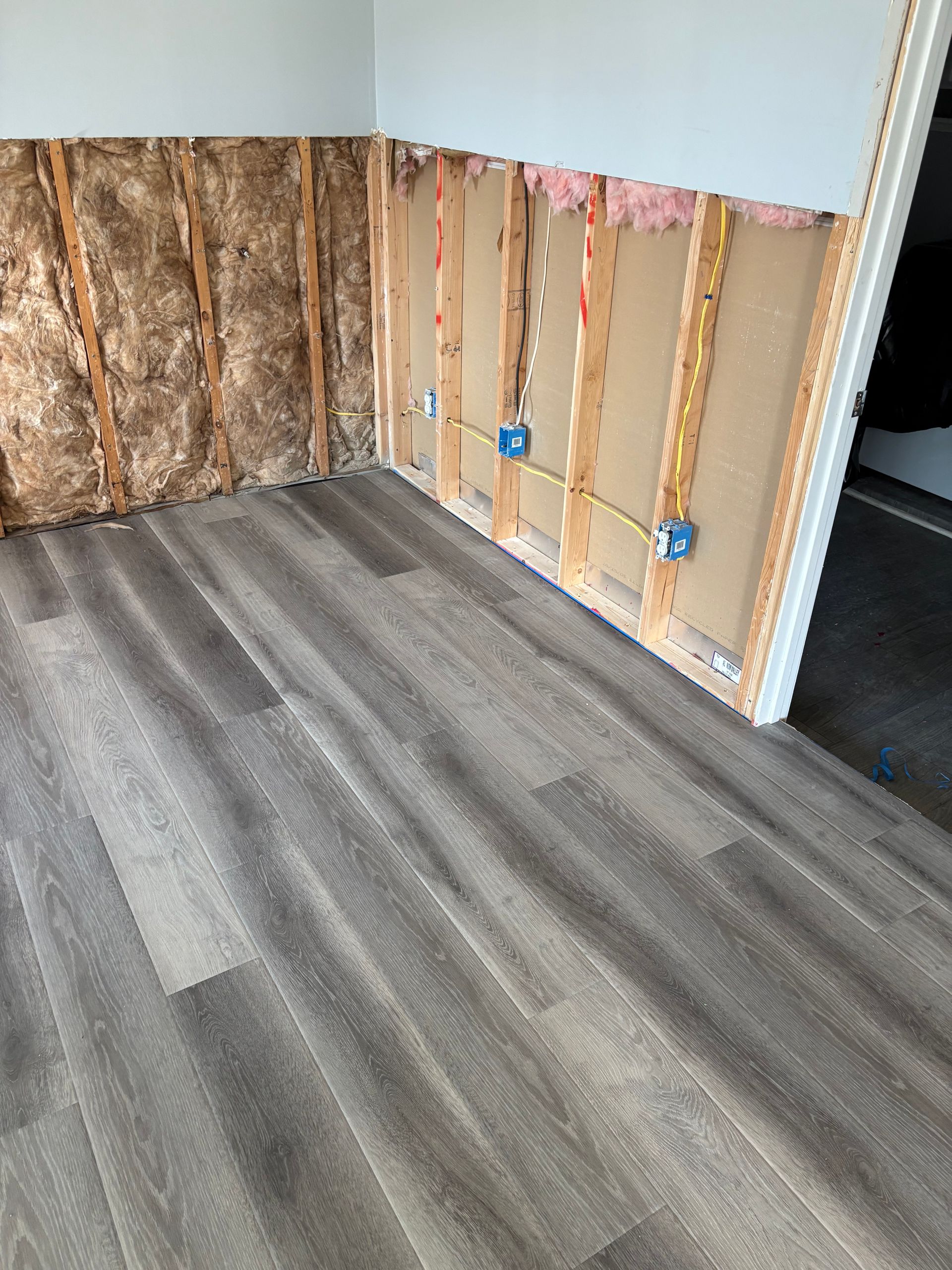 Partially renovated room with exposed wall studs and gray wood-look flooring