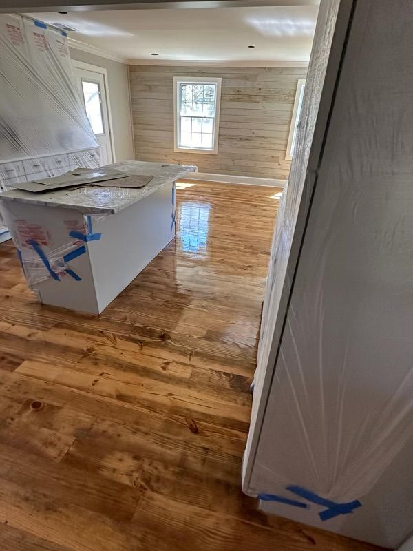 Partially furnished room with glossy hardwood floor, white-wrapped furniture, and a window at the far end