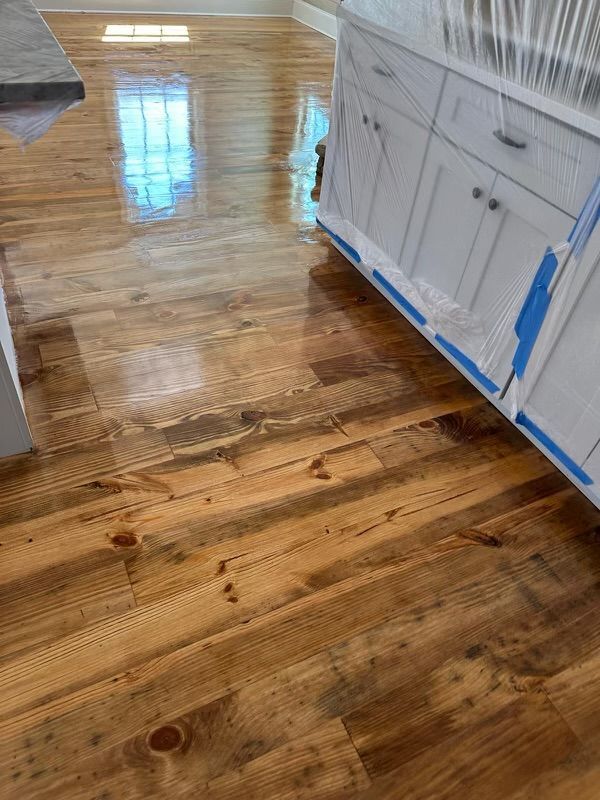 Shiny hardwood kitchen floor with blue painter’s tape along white cabinets and baseboards