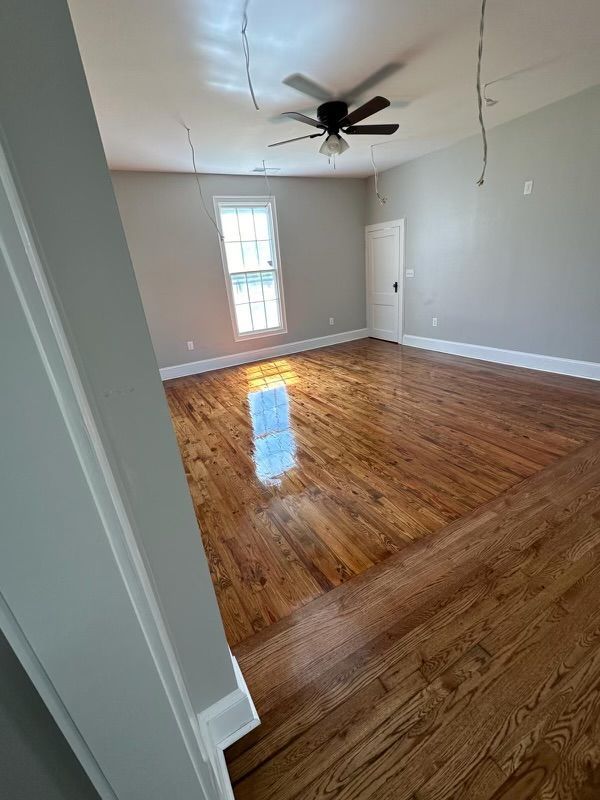 Empty room with hardwood floors, gray walls, a ceiling fan, and a single window.