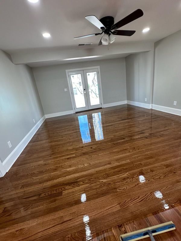 Empty living room with glossy hardwood floors, gray walls, ceiling fan, and French doors leading outside