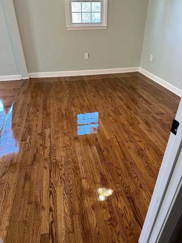 Empty room with glossy hardwood floor, gray walls, and a small window.