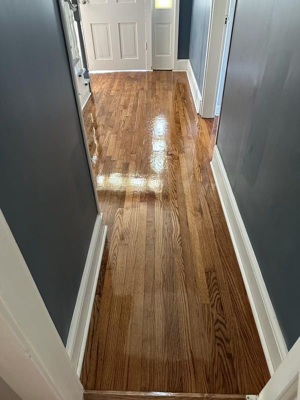 Narrow hallway with polished hardwood floor, gray walls, white trim, and a white door at the end.
