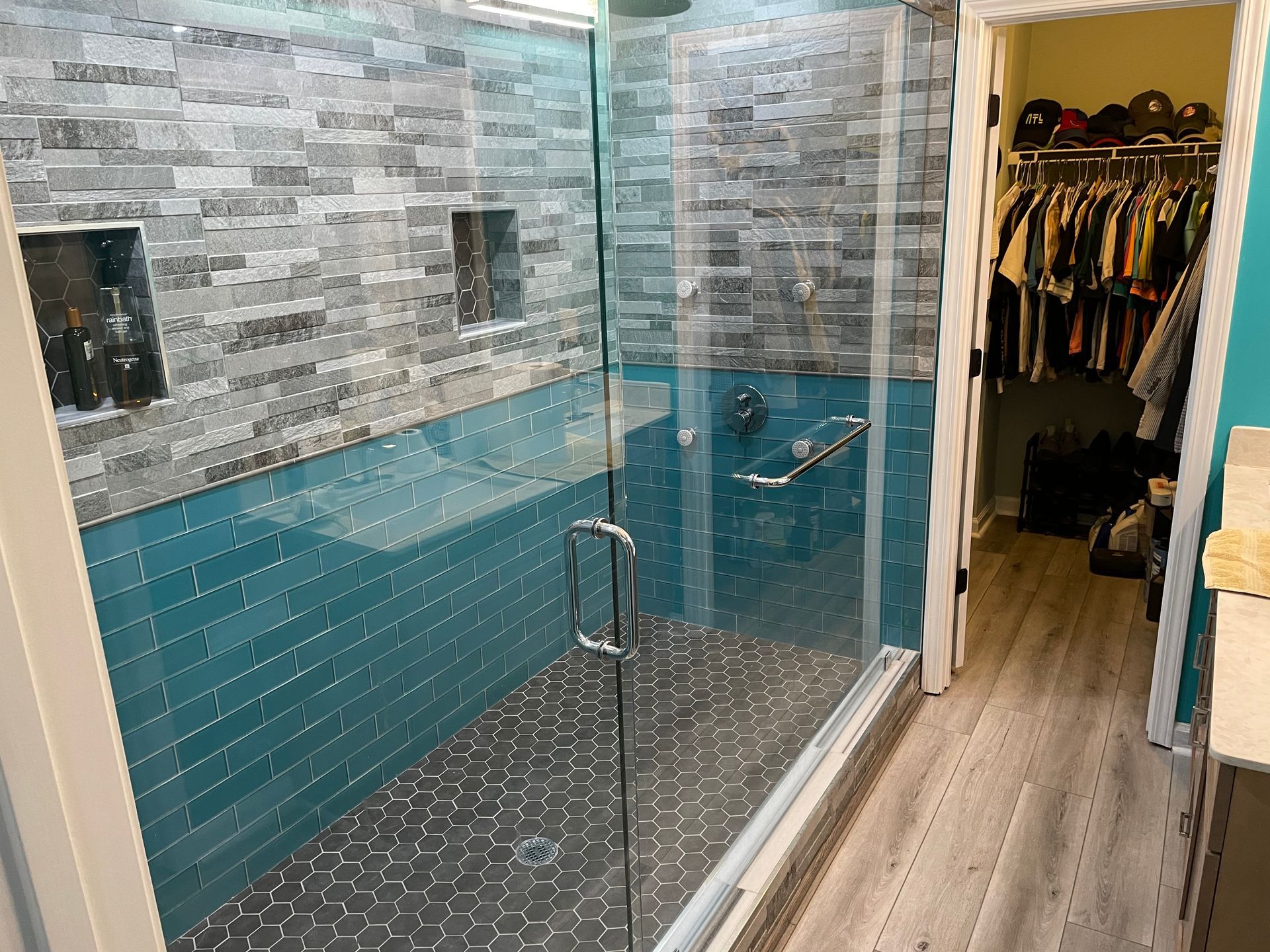 Glass shower enclosure with blue-tiled walls and a tiled bathroom floor, beside a walk-in closet.