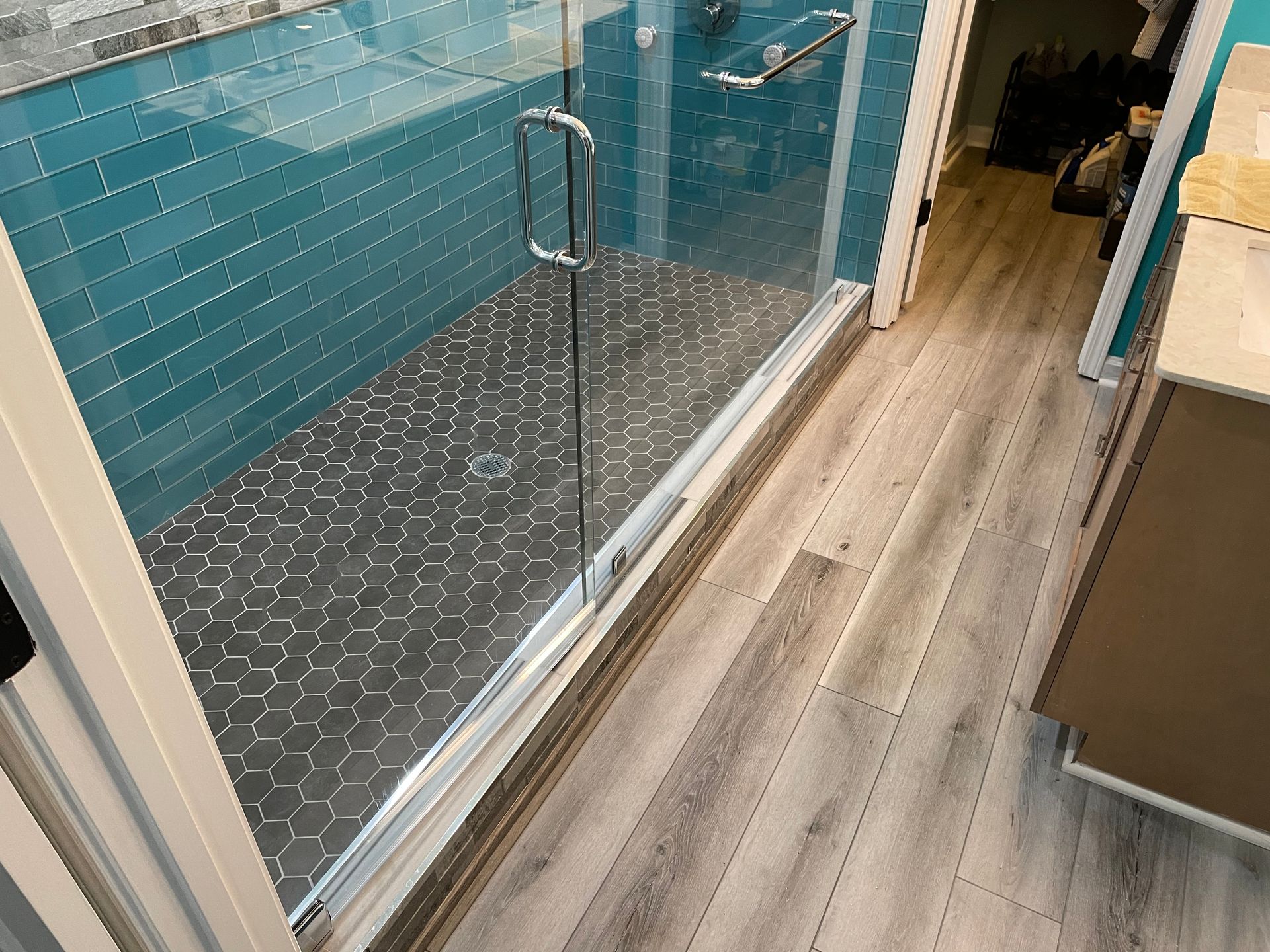 Glass shower enclosure with blue tile and wood-look bathroom floor beside a vanity
