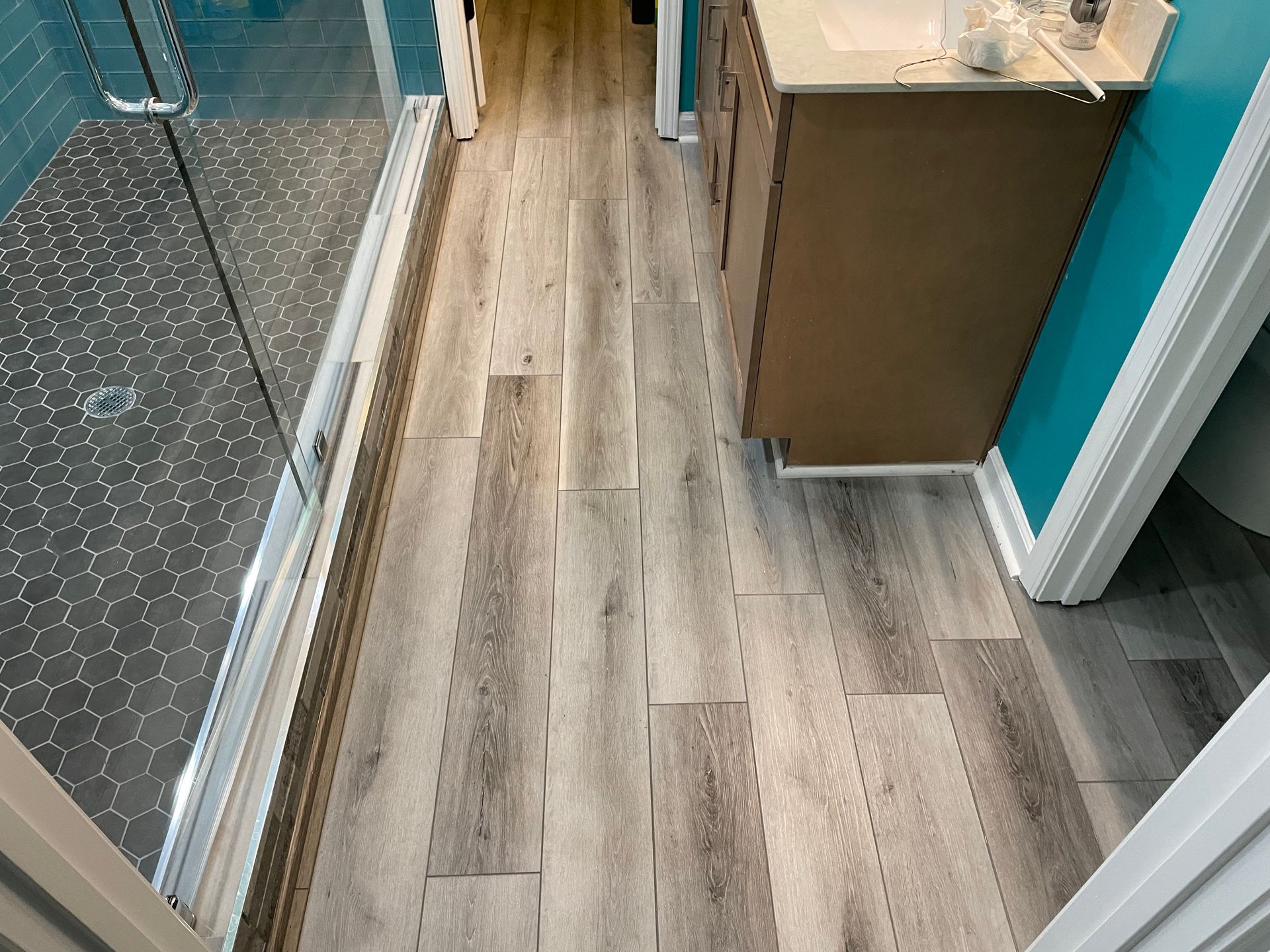 Narrow hallway with wood-look flooring, glass railing, and a small cabinet at the end
