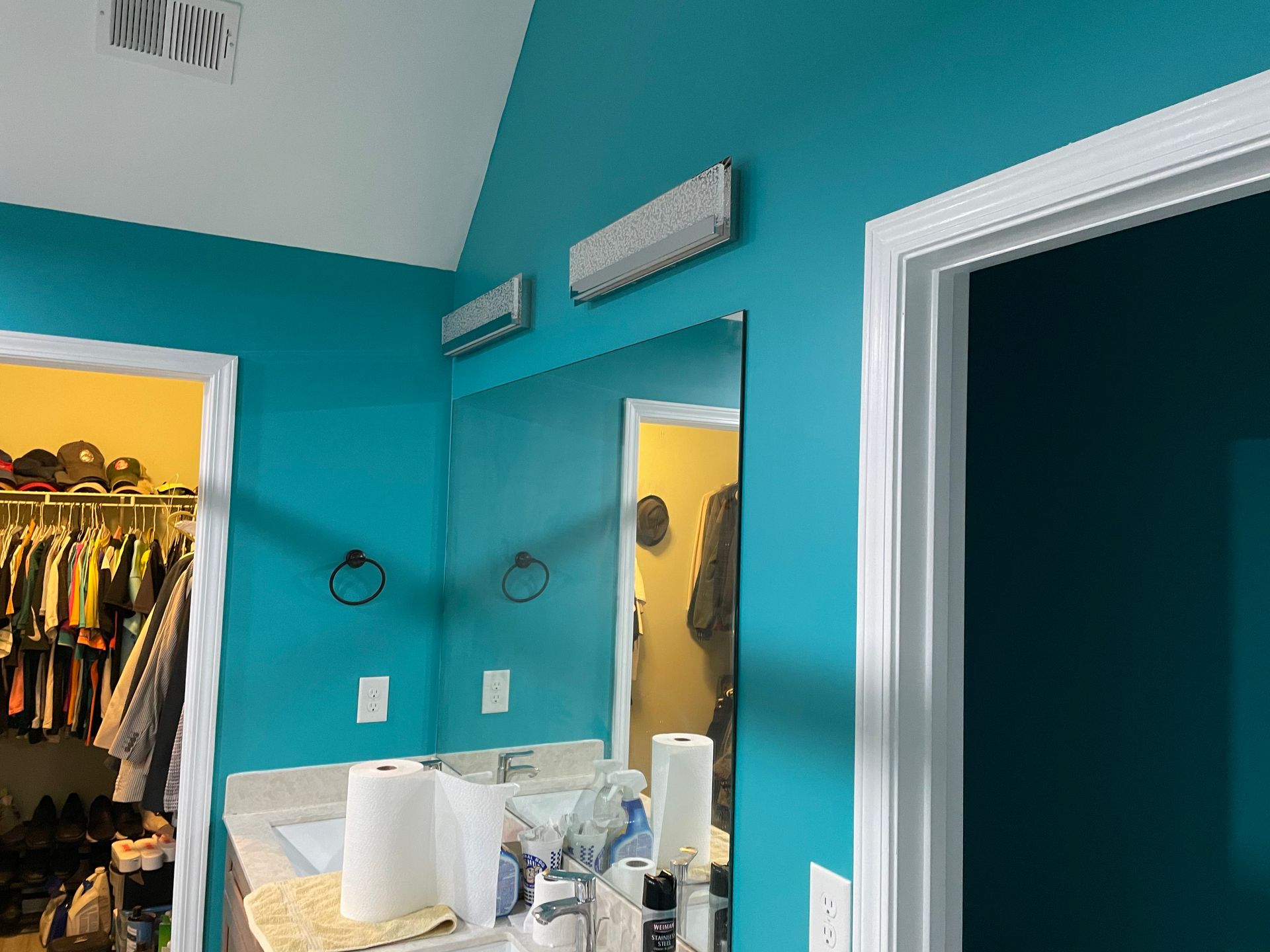 Teal bathroom vanity with mirrors and wall vents beside an open closet doorway