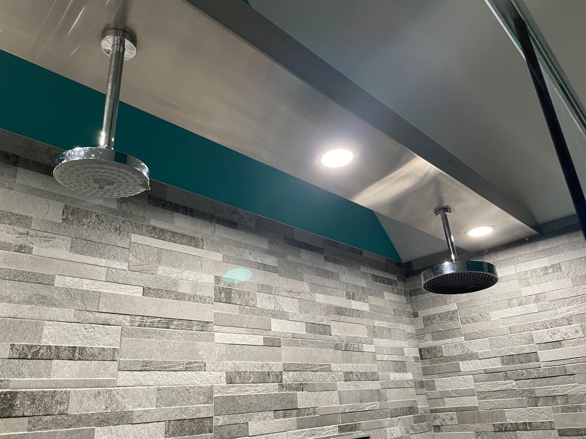 Bathroom with gray stone tile, teal accent wall, and two modern rainfall showerheads on the ceiling