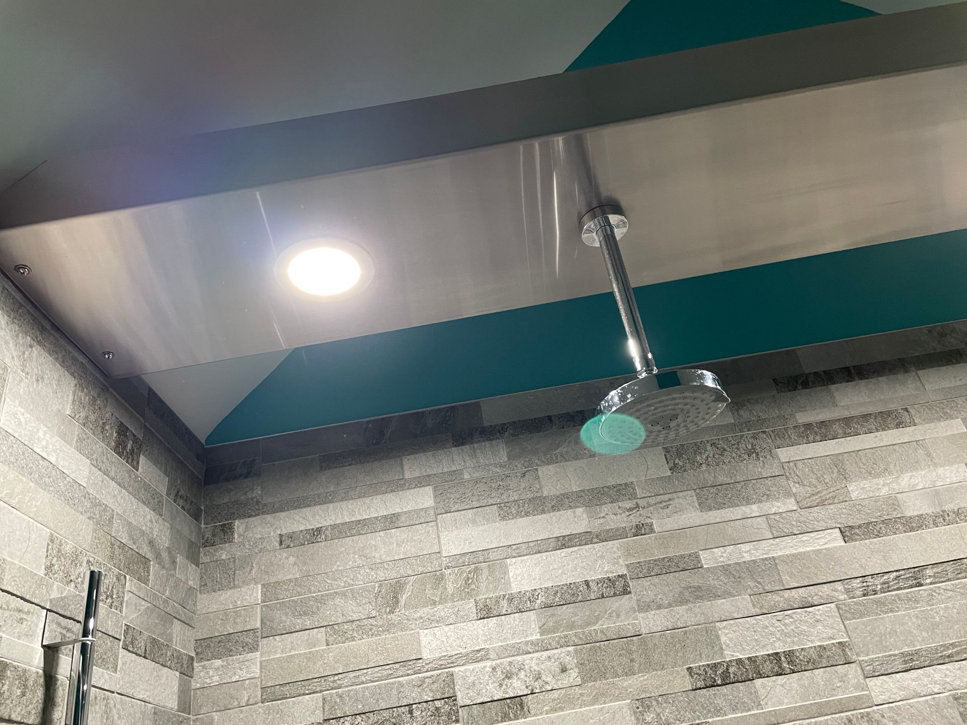 Tiled shower corner with a ceiling-mounted showerhead and recessed light.