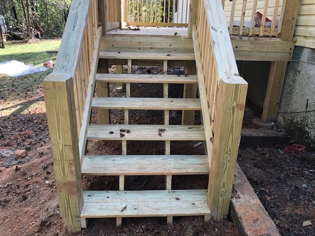 Wooden outdoor stairs with railings leading up to a deck, seen from the base.