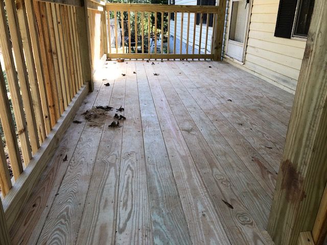 Wooden porch deck with scattered dirt, railings on the left, and a house wall on the right.
