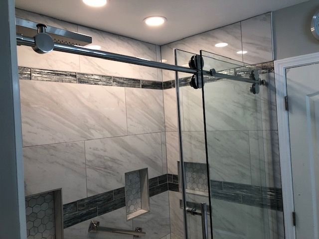 Glass shower enclosure with chrome sliding door and marble-tile walls