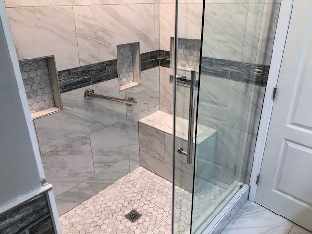 Modern tiled bathroom shower with glass door, white hex tile floor, and built-in bench shelves
