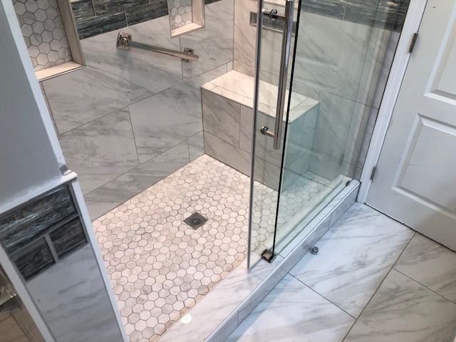 Modern bathroom with glass shower enclosure, white marble tile floor, and pebble shower base