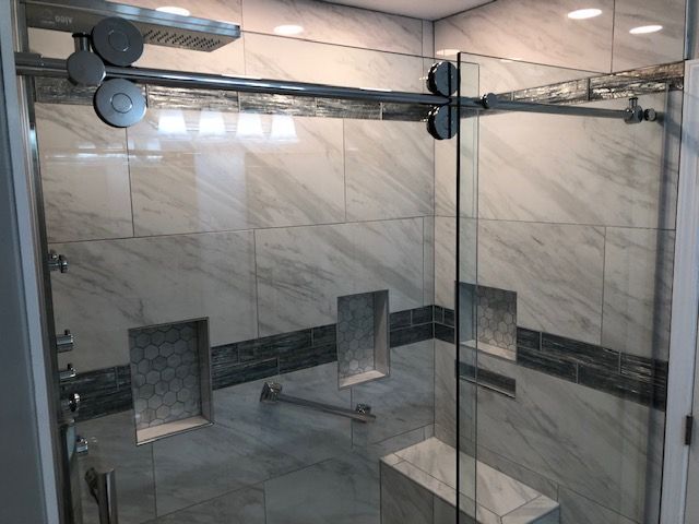 Modern tiled shower with glass doors, marble walls, and built-in seating shelves