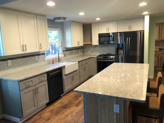 Modern kitchen with white cabinets, gray countertops, stainless appliances, and a large island with wood floor