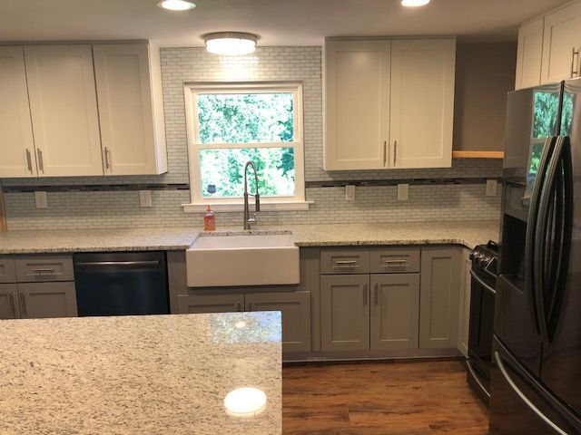 Modern kitchen with white cabinets, granite island, farmhouse sink under window, and stainless steel appliances