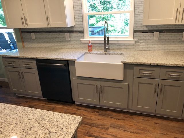 Kitchen with gray cabinets, white countertops, farmhouse sink, and window above the sink