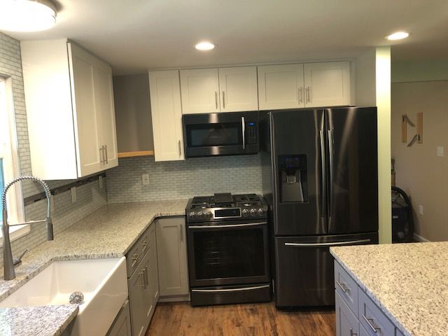 Modern kitchen with white cabinets, granite counters, stainless fridge, stove, microwave, and sink near a window.