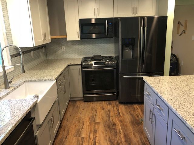 Modern kitchen with white cabinets, granite countertops, black appliances, and wood flooring.