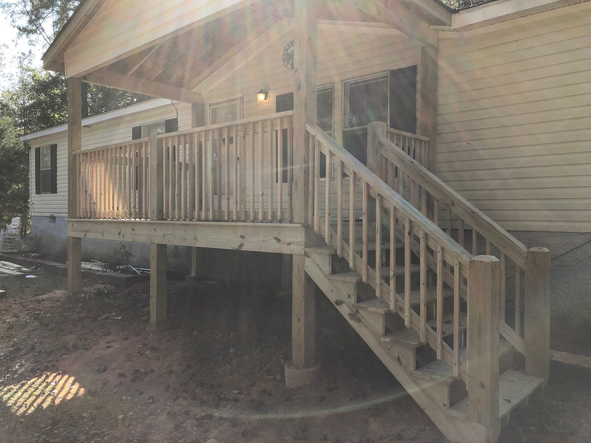 Wooden raised porch with railing and stairs attached to a beige house in a wooded yard