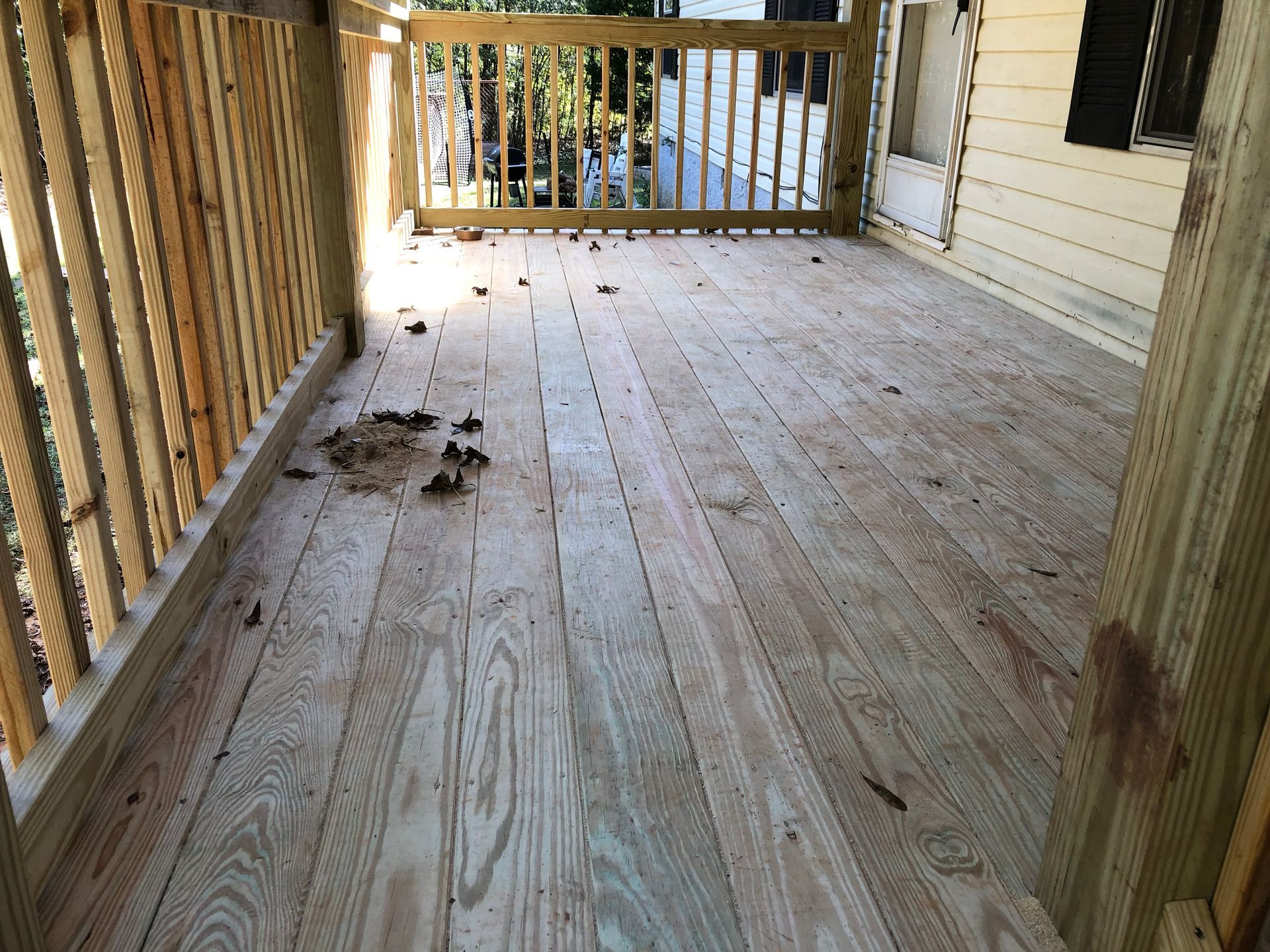 Wooden porch with scattered dirt and debris, railings on the left and at the end, and a house wall on the right