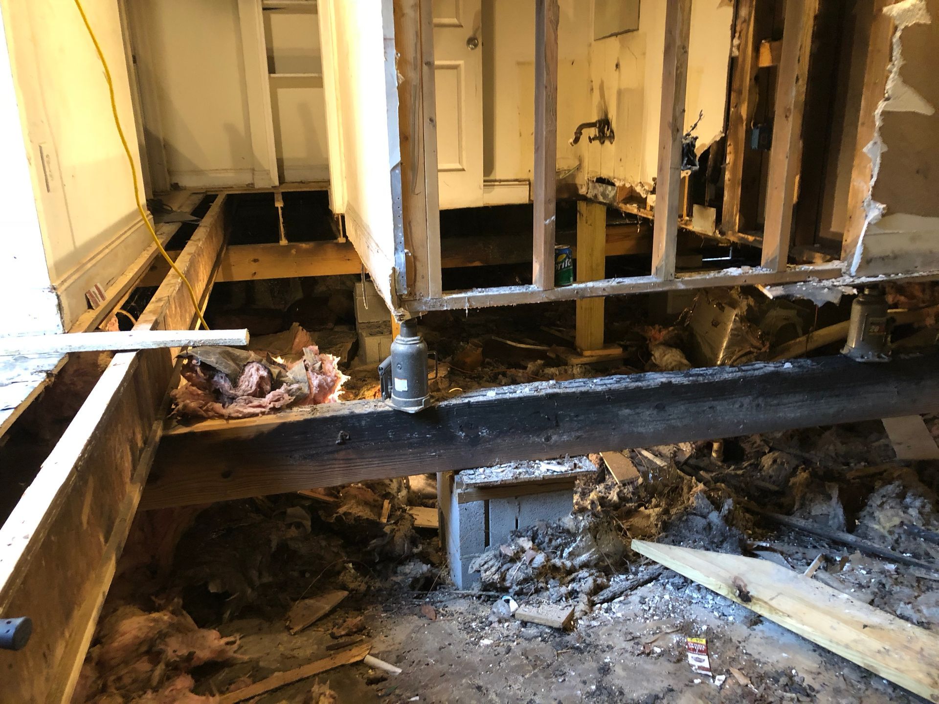 Exposed floor joists and debris in a gutted room with damaged walls and subfloor removed