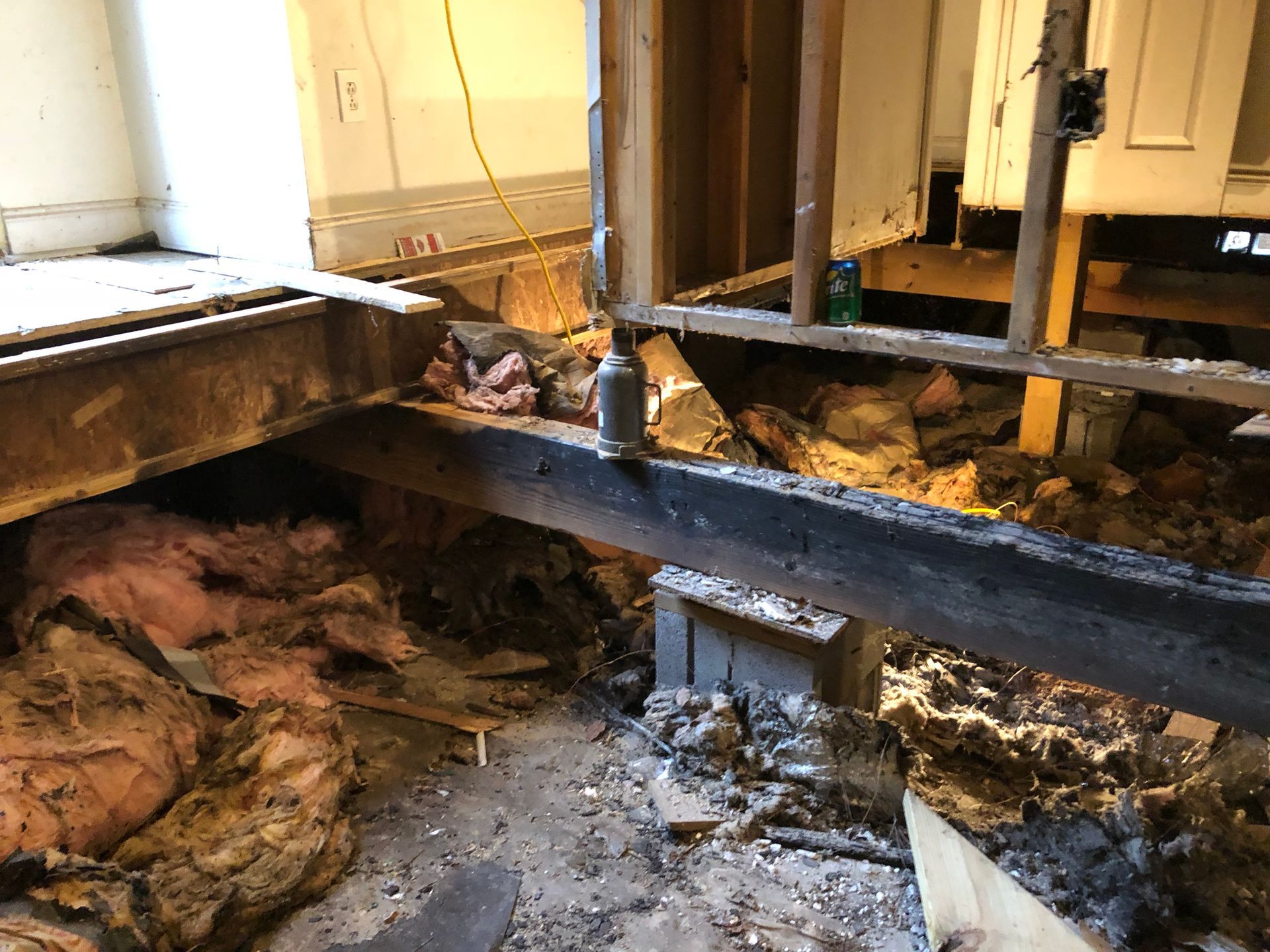 Flood-damaged room with exposed floor joists, insulation, and debris under a raised black beam.