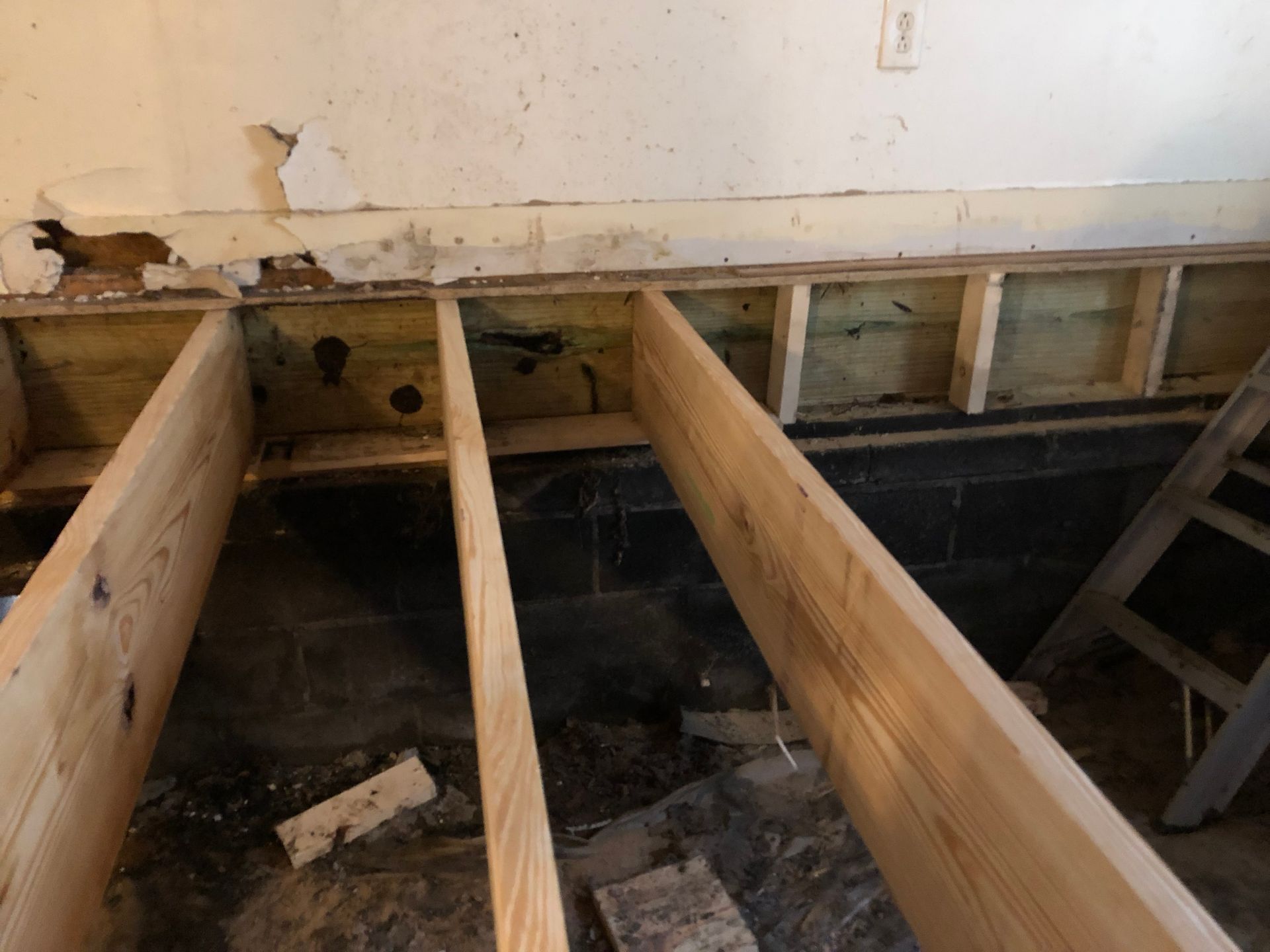 Exposed floor joists and damaged wall framing in a room under renovation