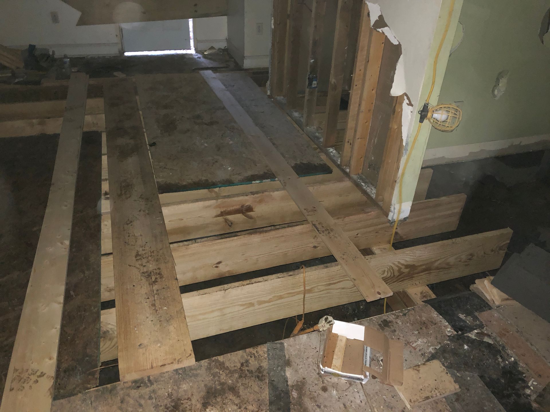 Damaged floor with exposed wooden joists and loose boards in a dim interior room