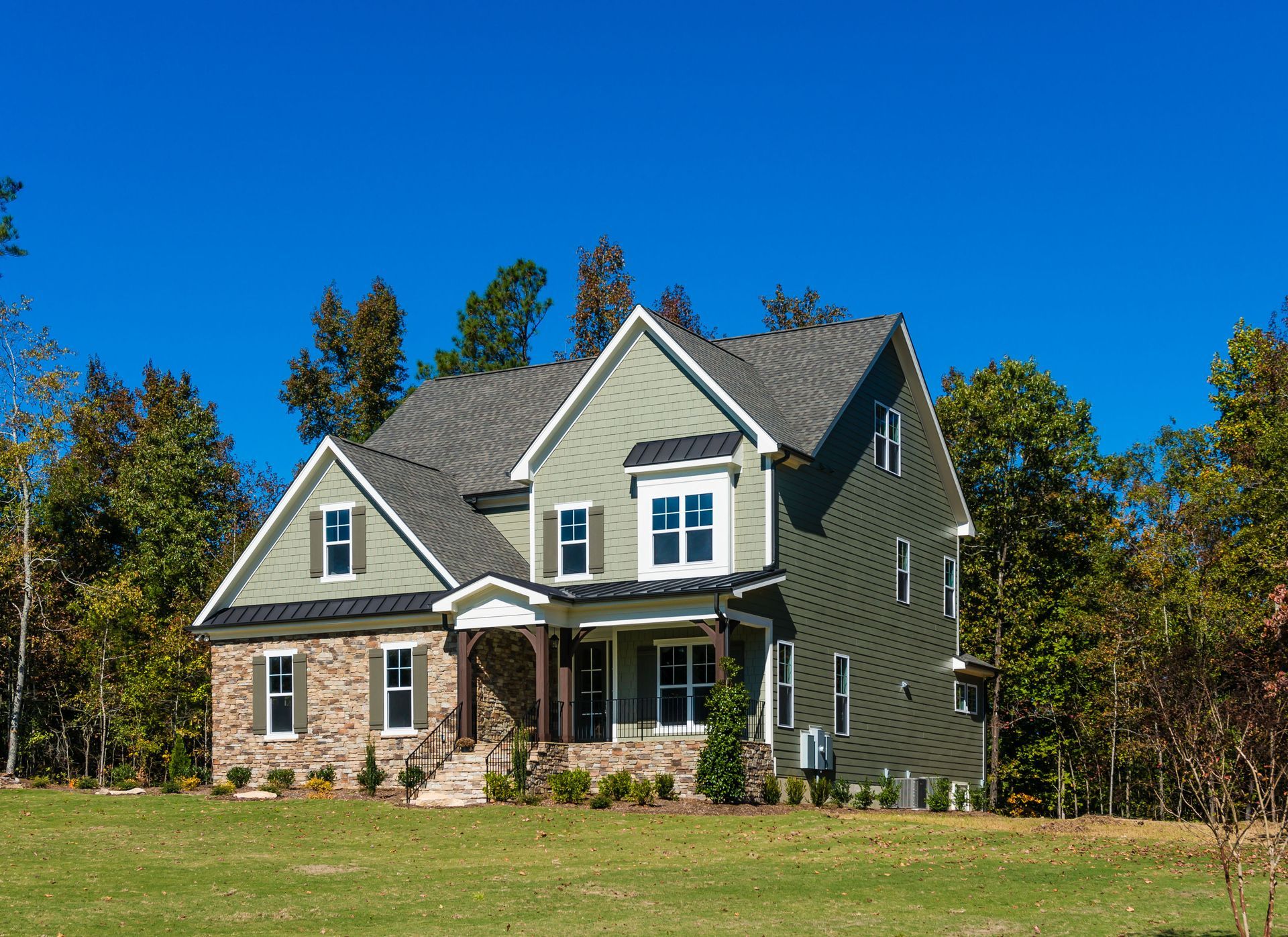 Two-story suburban house with stone and green siding under a clear blue sky