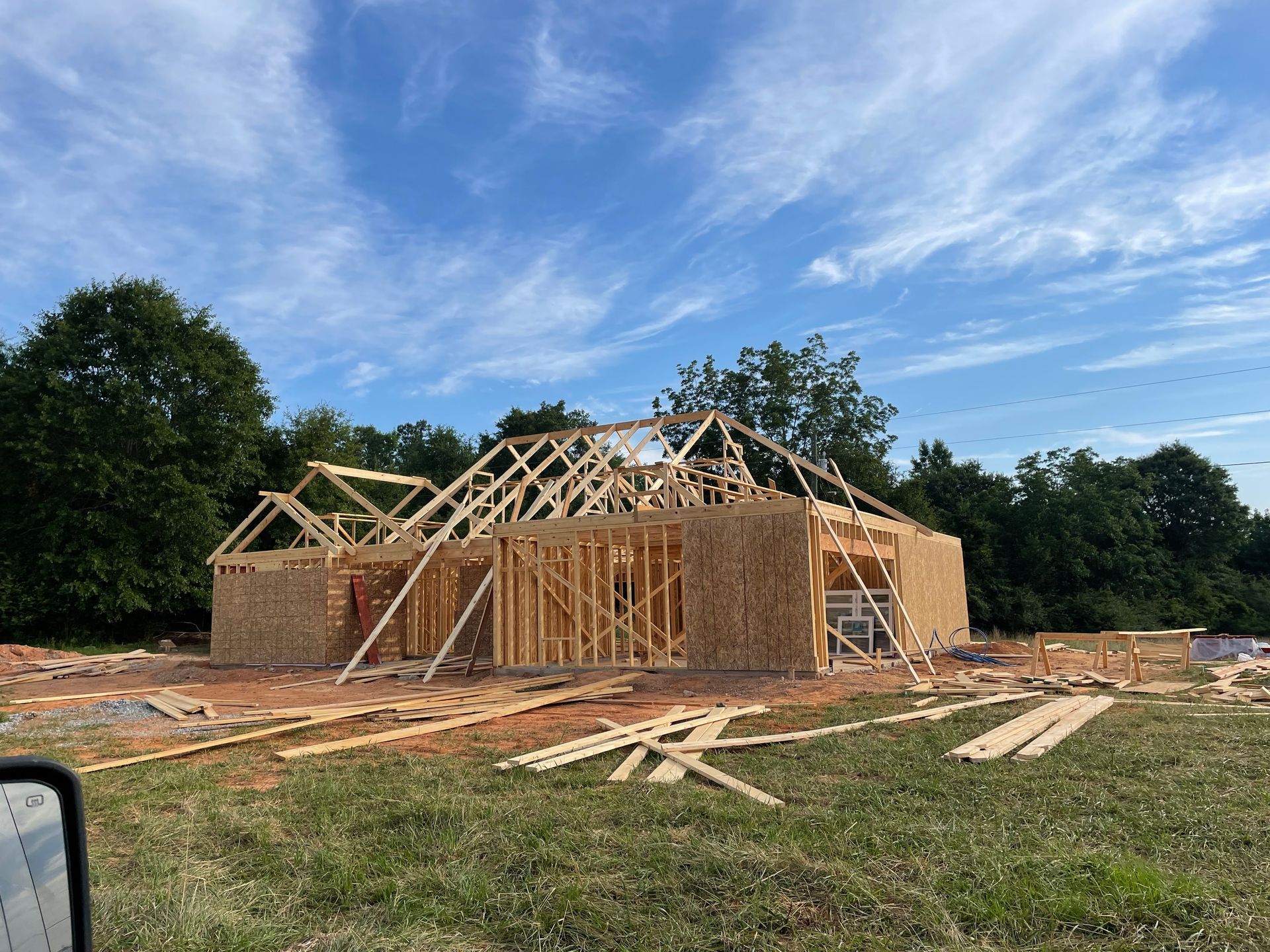 Partially framed house under construction on a grassy lot with blue sky overhead