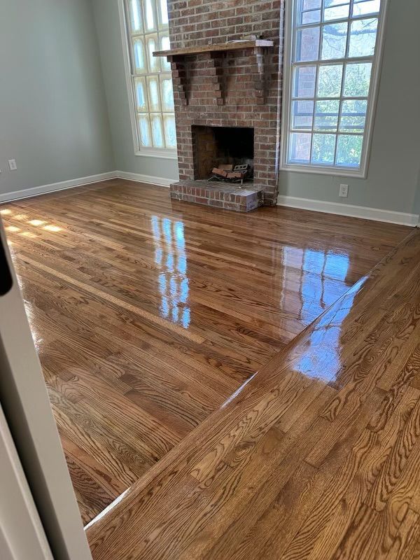 Empty room with glossy hardwood floors and a brick fireplace between tall windows