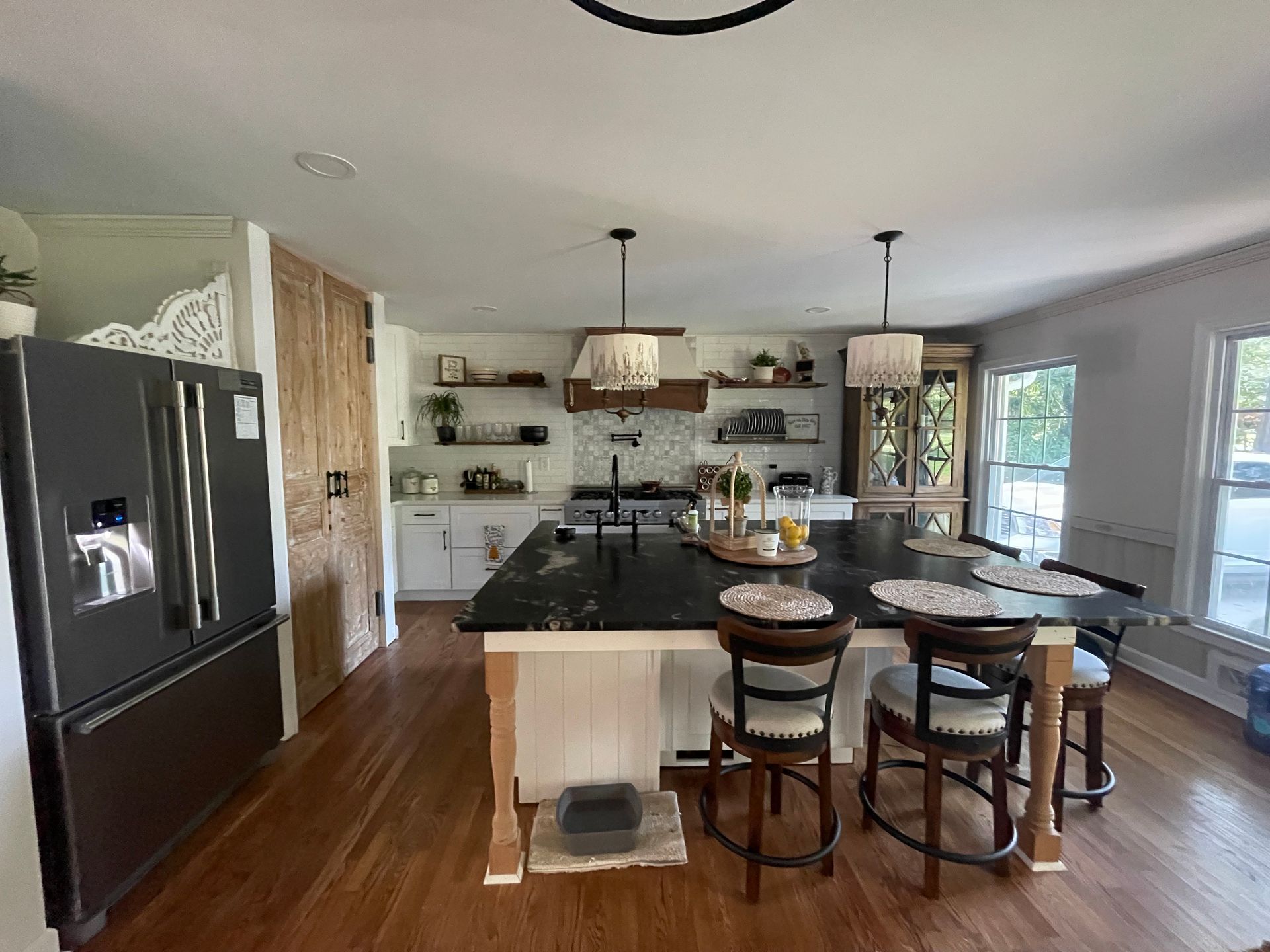 Modern kitchen with black refrigerator, island, dining table, and large windows overlooking a bright living area
