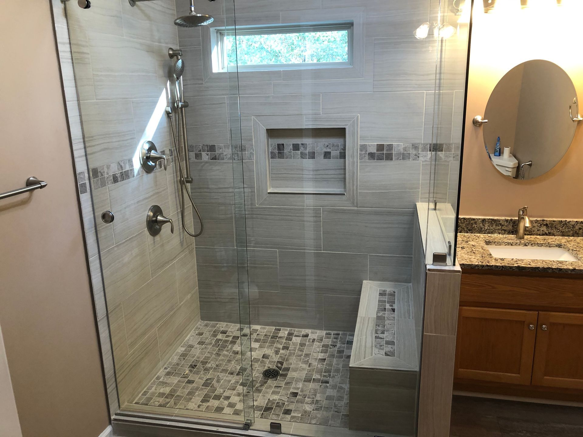Modern walk-in shower with gray tile, mosaic floor, glass panel, and built-in bench in a bathroom
