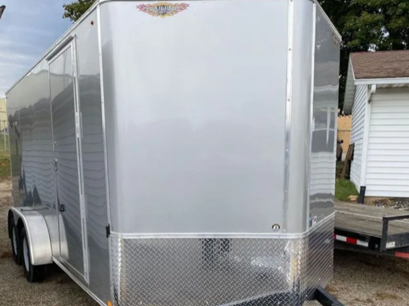 Silver enclosed cargo trailer with diamond plate front panel, parked outdoors