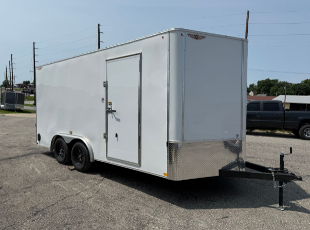 White enclosed cargo trailer on a paved lot with a parked truck in the background.