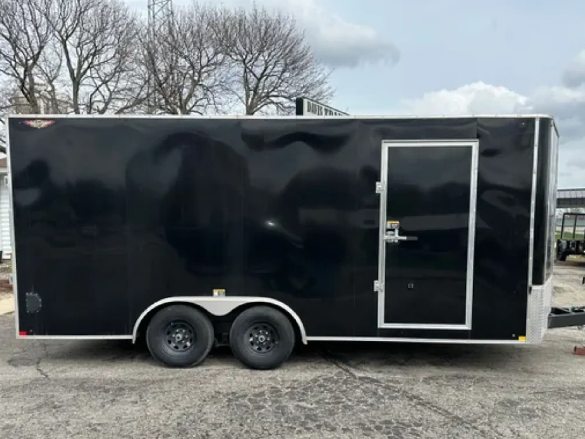 Black dump trailer parked in front of a white building with a sign.