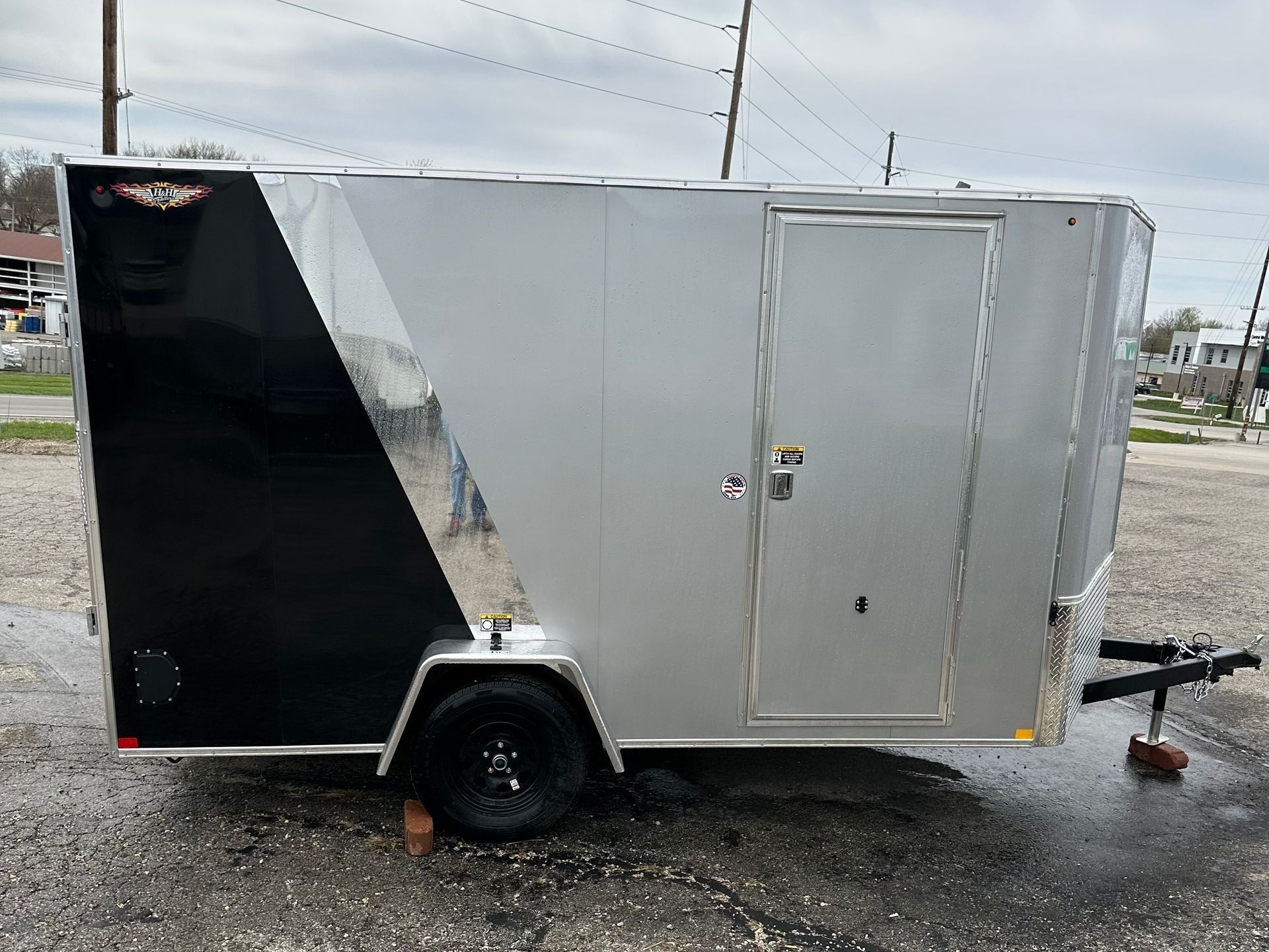 Silver and black enclosed trailer parked outdoors on a cloudy day.