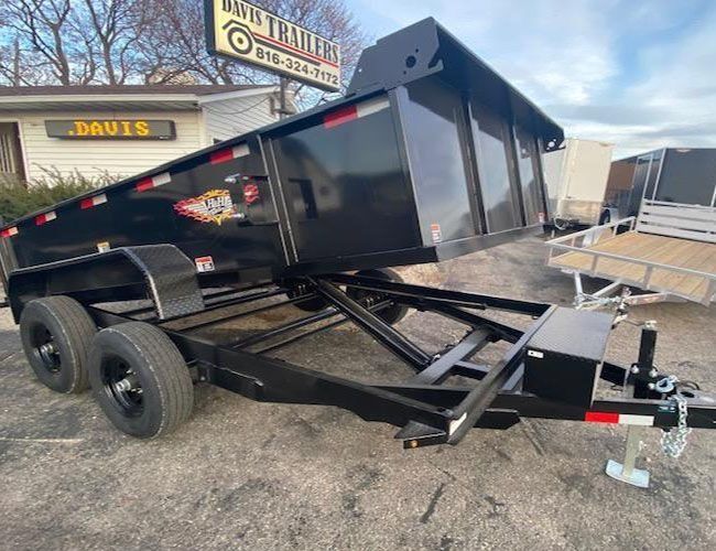 Black dump trailer parked in front of a building with a business sign.