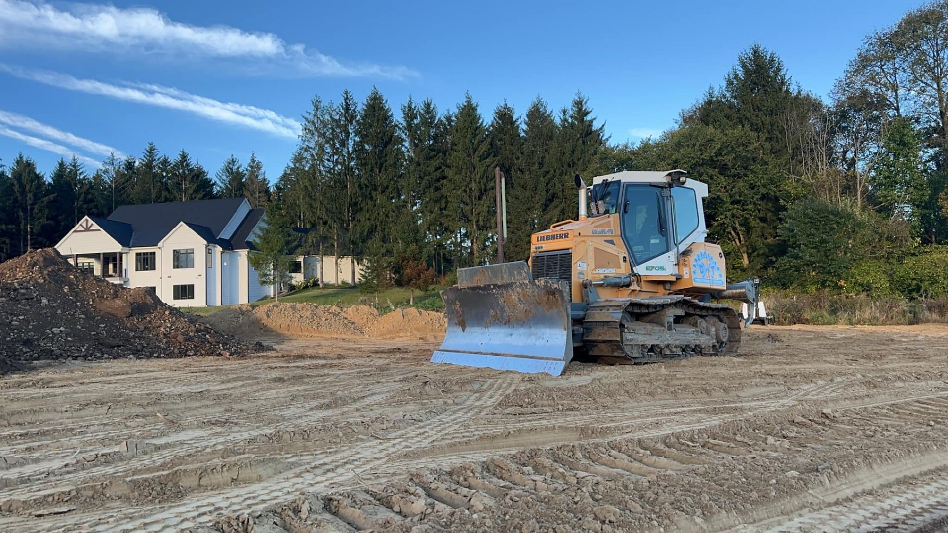 A bulldozer is driving through a dirt field in front of a house.