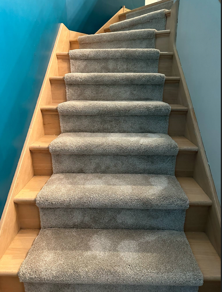 Staircase with light wood steps and gray carpet treads, leading upwards against a teal wall.