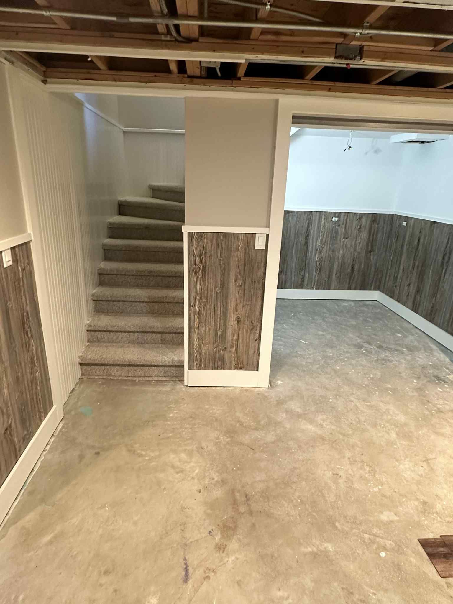 Basement with stairs, wood paneling, exposed ceiling beams, and concrete floor.