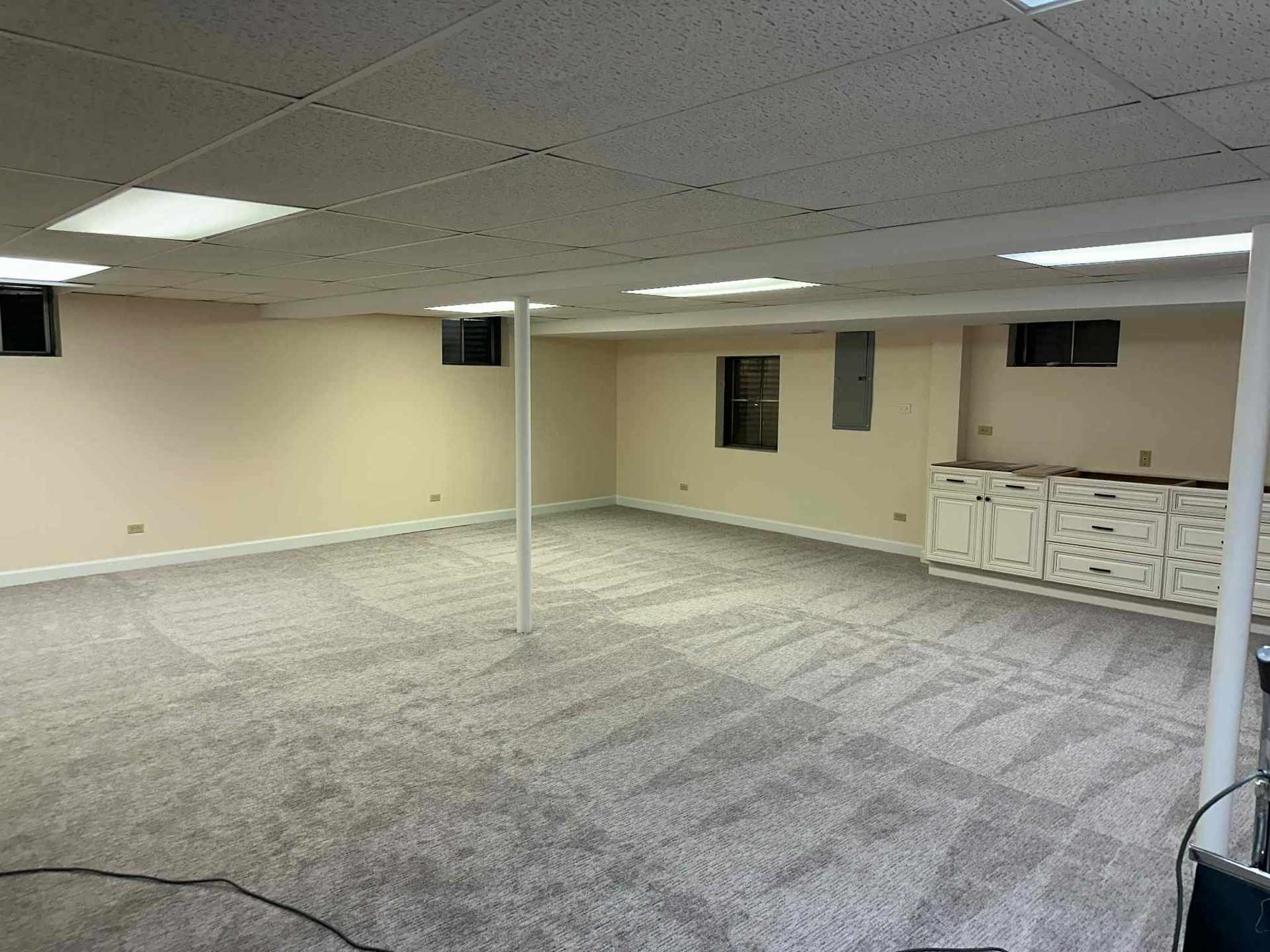 Empty basement with light gray carpet, beige walls, and white support beams.