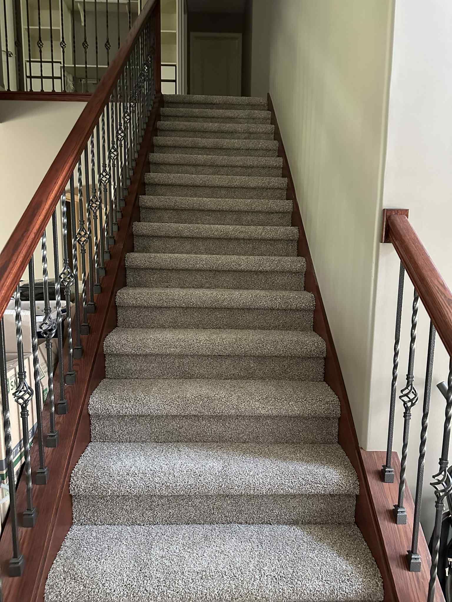 Staircase with brown wooden handrails and carpeted steps, leading upwards towards a hallway.