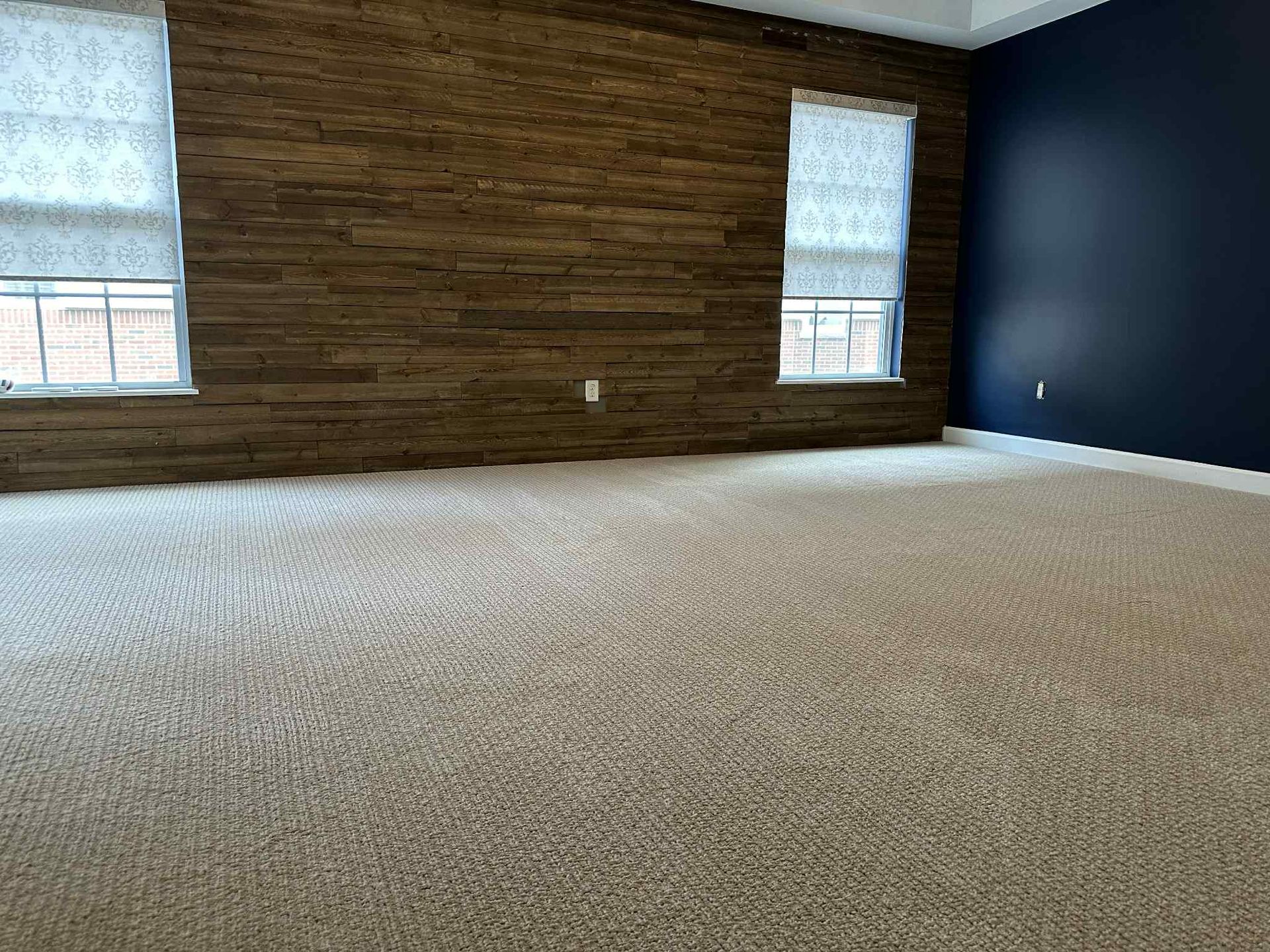 Empty bedroom with beige carpet, two windows with blinds, wood accent wall, and a blue wall.