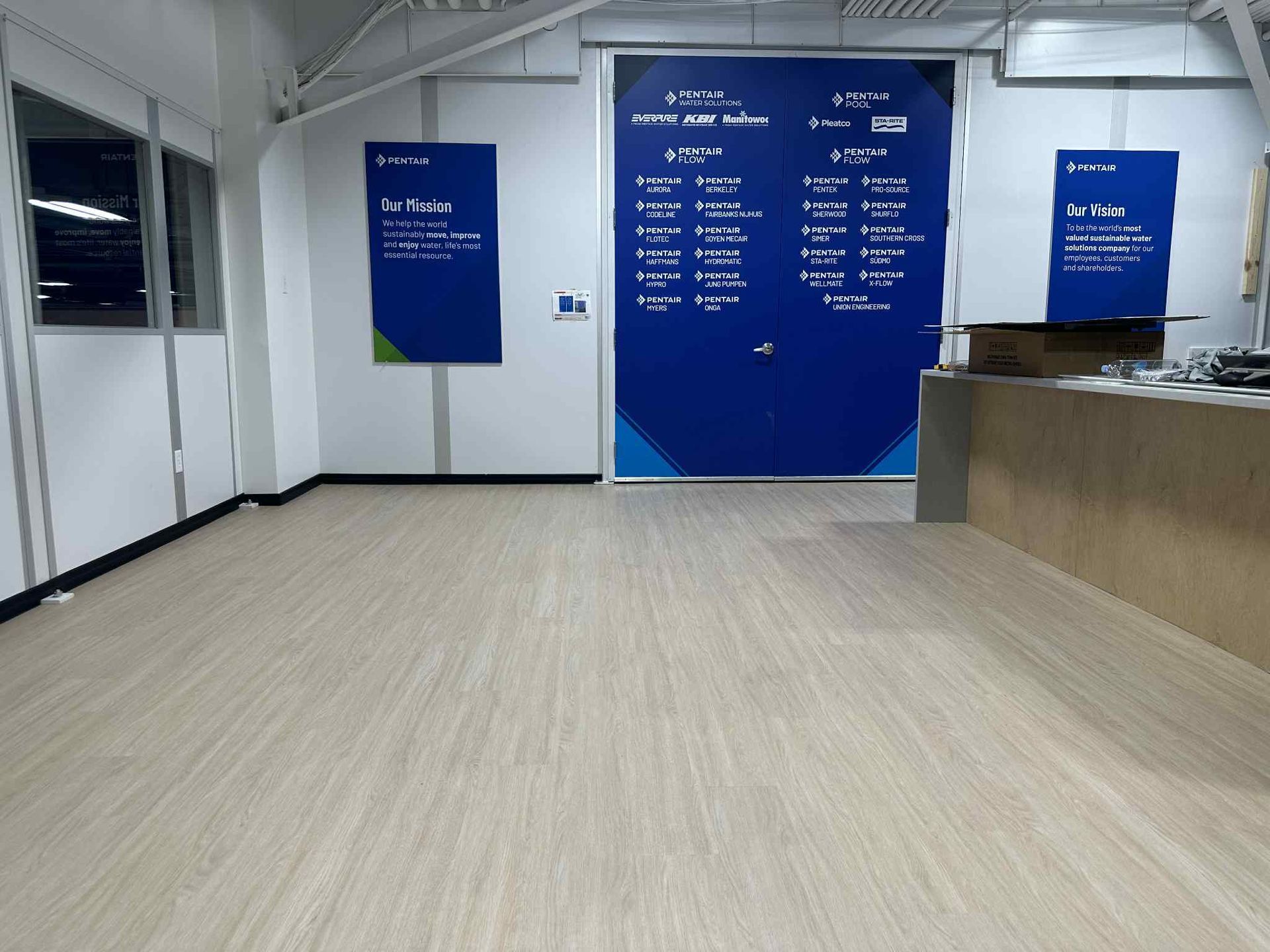 Empty room with light wood flooring, blue doors and posters, and white walls.