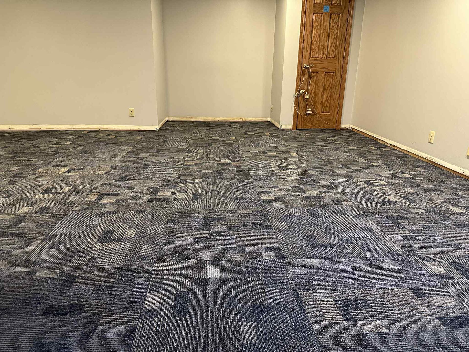 Room with blue and gray patterned carpet, gray walls, and a textured brown door.
