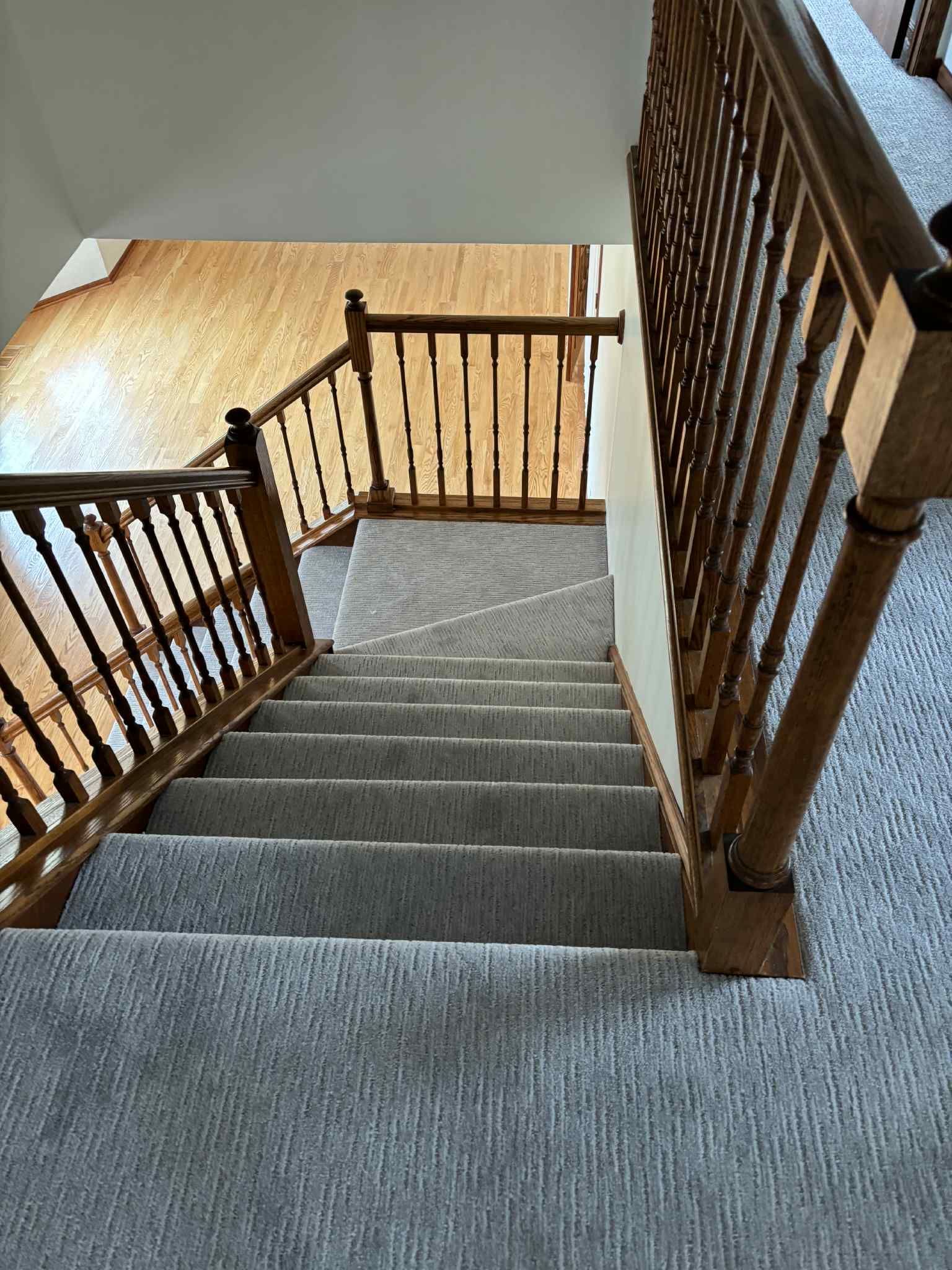 Staircase with gray carpet and wooden railing descending to a wood floor.