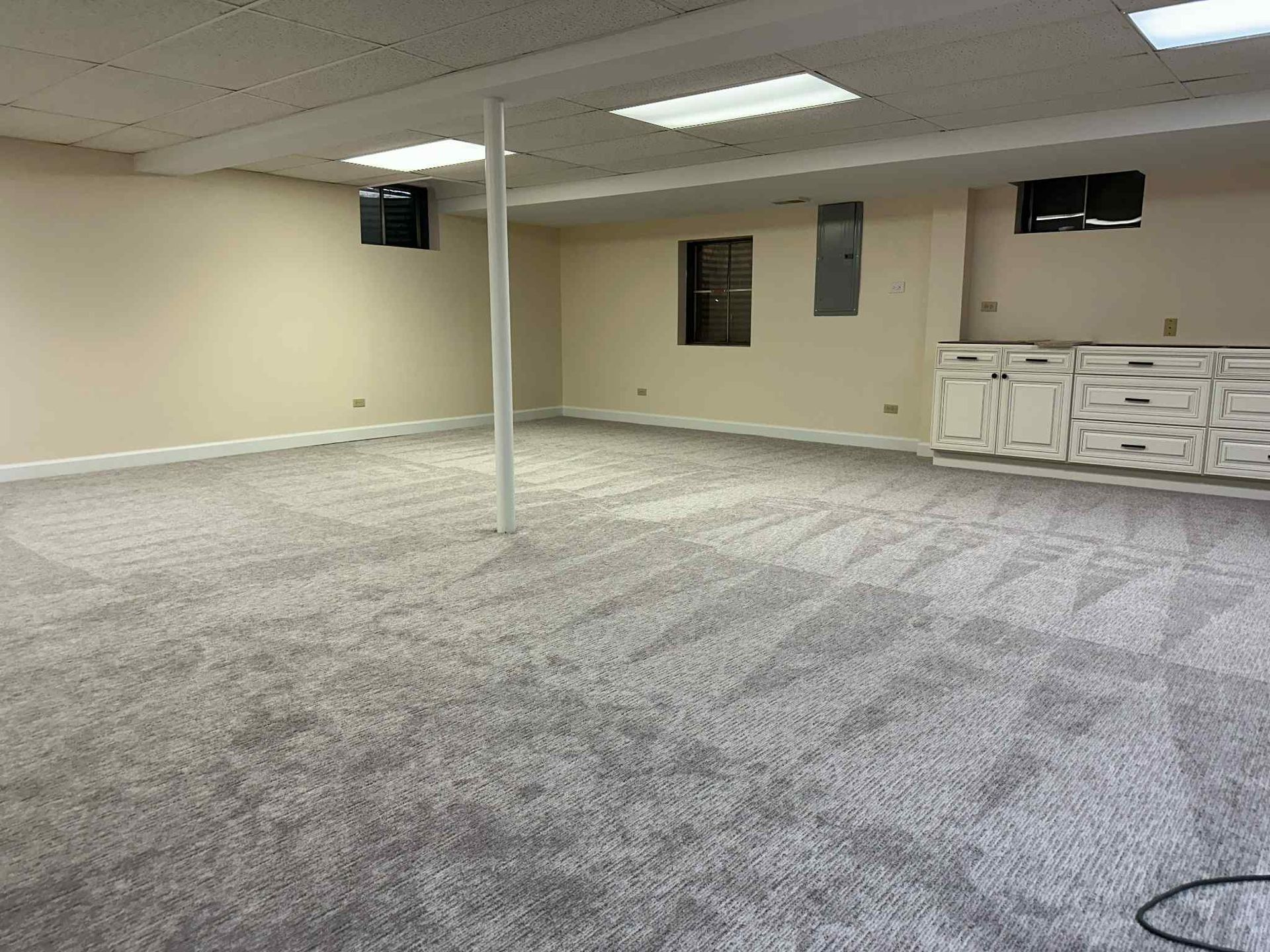 Empty, carpeted room with beige walls, a support beam, and built-in cabinets.